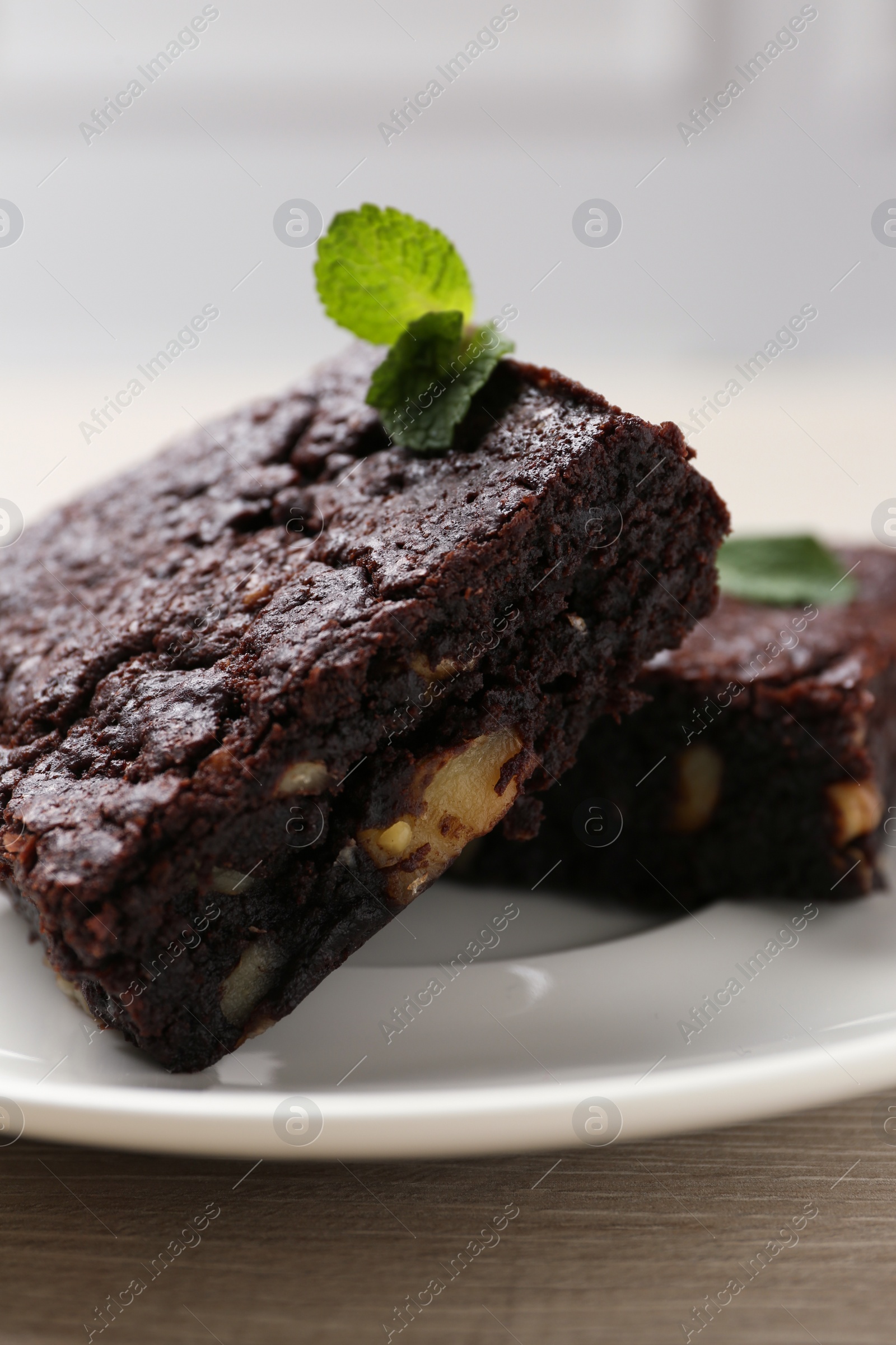 Photo of Delicious brownies with nuts and mint on wooden table, closeup