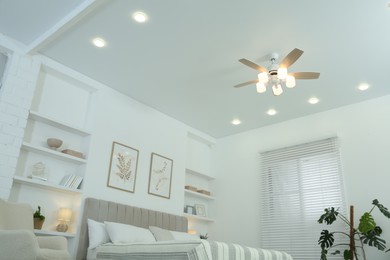 Comfortable furniture, ceiling fan, houseplants and accessories in stylish bedroom, low angle view