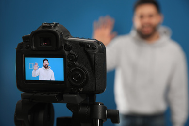 Young blogger shooting video with camera against blue background, focus on screen