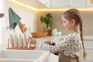 Photo of Girl putting clean plate on drying rack in kitchen