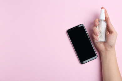 Photo of Woman with smartphone and antiseptic spray on pink background, top view. Space for text