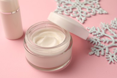 Winter skin care. Hand cream near snowflakes and cosmetic product on pink background, closeup