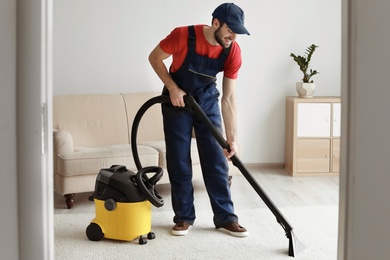 Male worker cleaning carpet with vacuum in living room