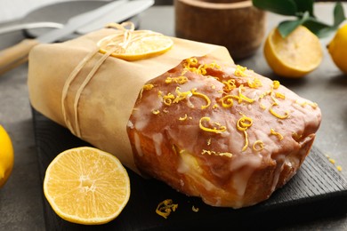 Wrapped tasty lemon cake with glaze and citrus fruits on grey table, closeup