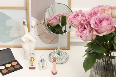 Photo of Mirror, cosmetic products, perfumes and vase with pink roses on white dressing table