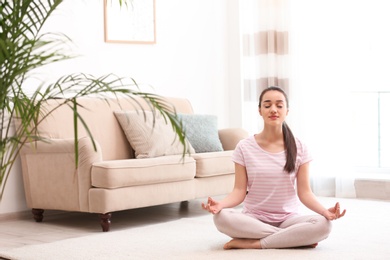 Photo of Young woman meditating on floor in living room, space for text. Zen concept