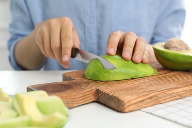 Photo of Woman cutting ripe avocado at table, closeup