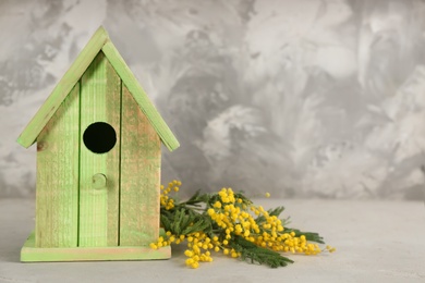 Beautiful bird house and mimosa flowers on light grey stone table, space for text