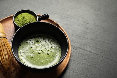 Photo of Cup of fresh matcha tea, bamboo whisk and green powder on black table, space for text