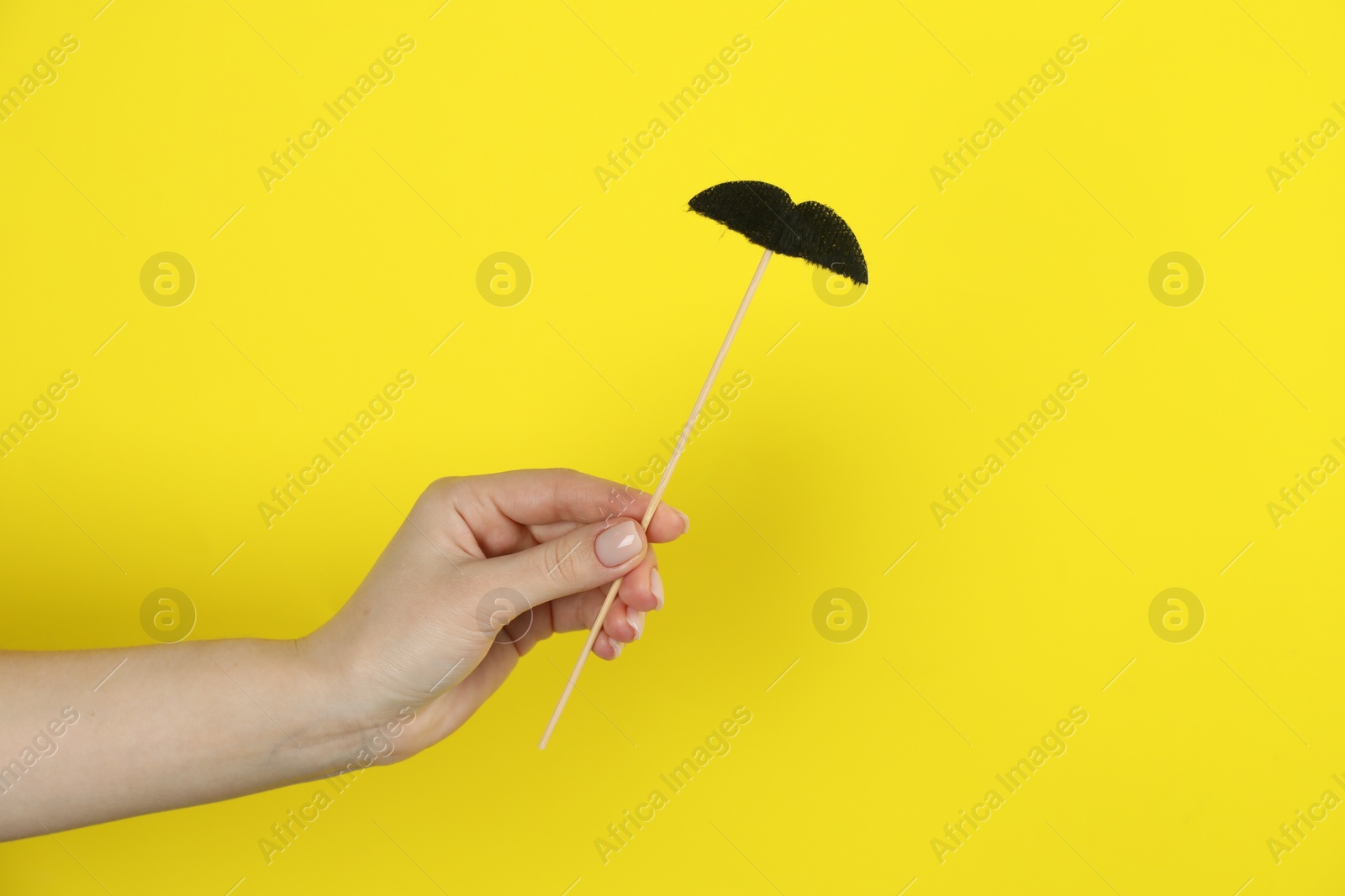 Photo of Woman with fake paper mustache on yellow background, closeup