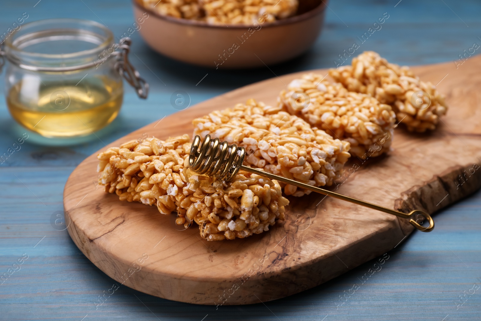 Photo of Board with puffed rice bars (kozinaki) on light blue wooden table, closeup