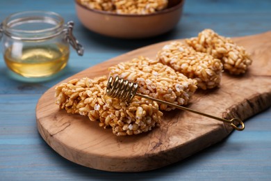 Photo of Board with puffed rice bars (kozinaki) on light blue wooden table, closeup