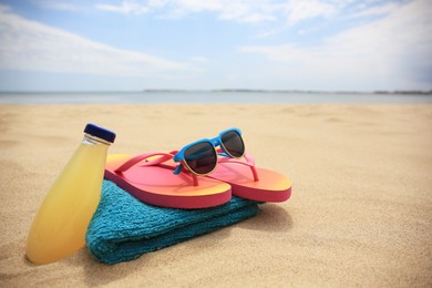 Photo of Stylish sunglasses, flip flops. towel and bottle of refreshing drink on beach, space for text