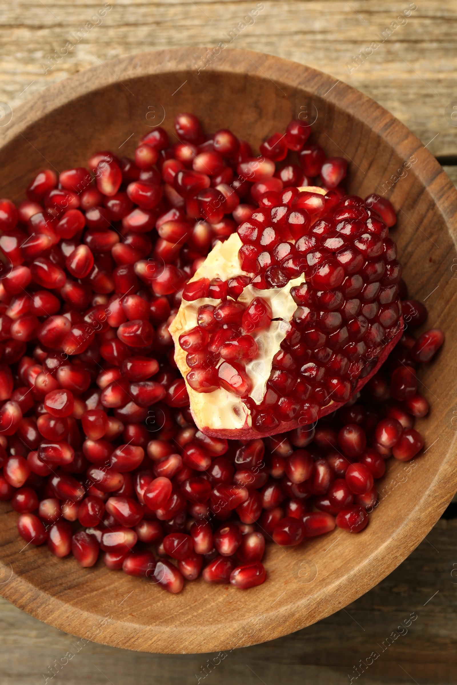 Photo of Ripe juicy pomegranate grains in bowl on wooden table, top view