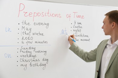 Photo of English teacher giving lesson on prepositions of time near whiteboard in classroom