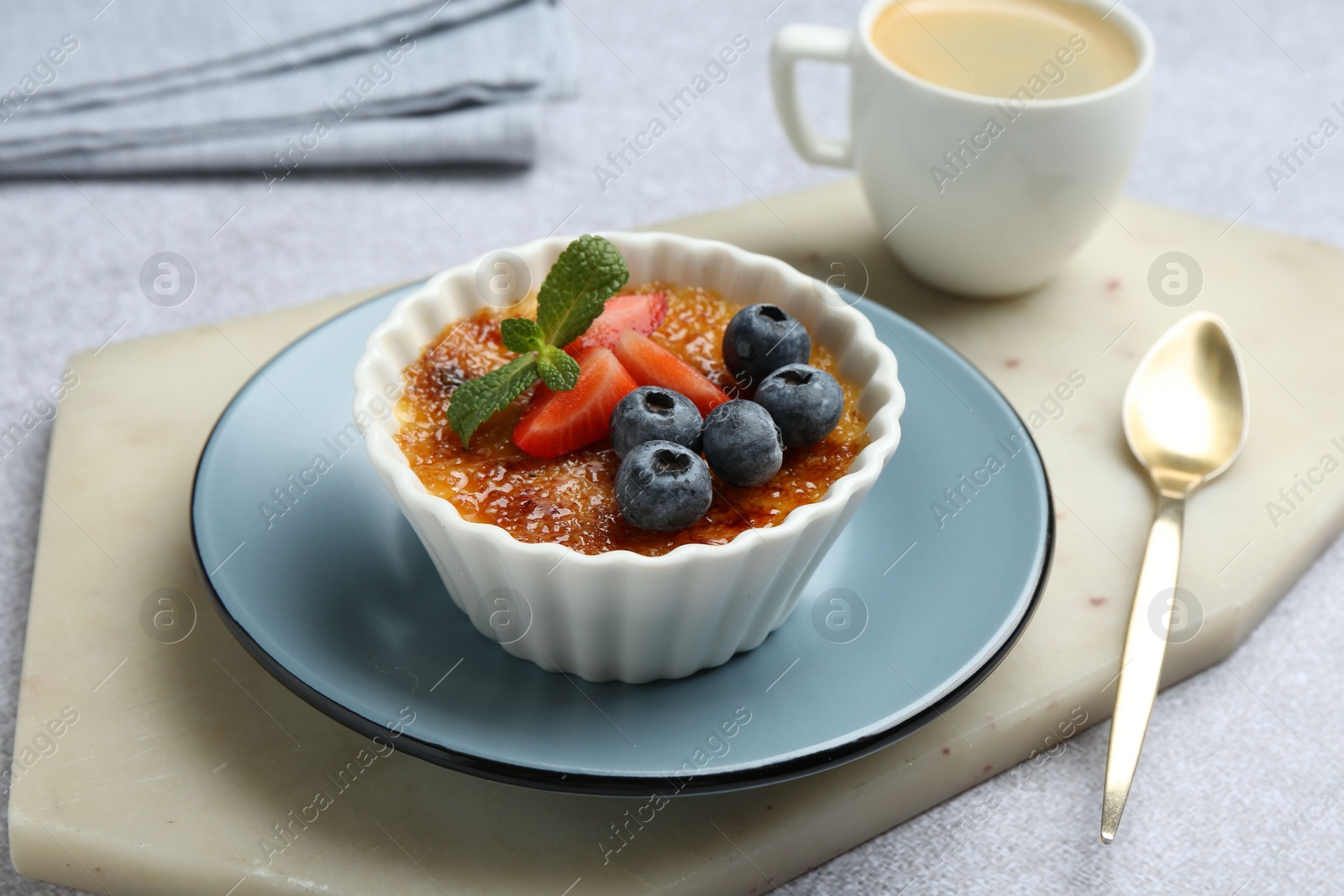 Photo of Delicious creme brulee with berries and mint in bowl served on grey table, closeup