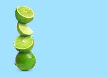 Stacked cut and whole limes on light blue background, space for text