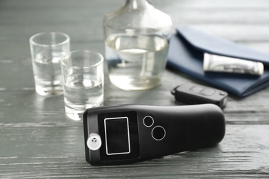 Photo of Modern breathalyzer, car key, alcohol and wallet on grey wooden background