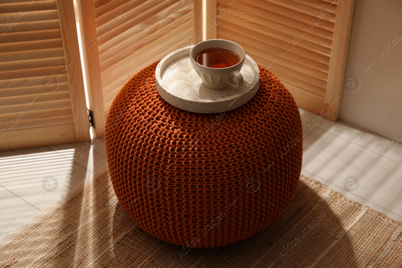 Photo of Tray with cup of tea on stylish comfortable pouf in room. Home design