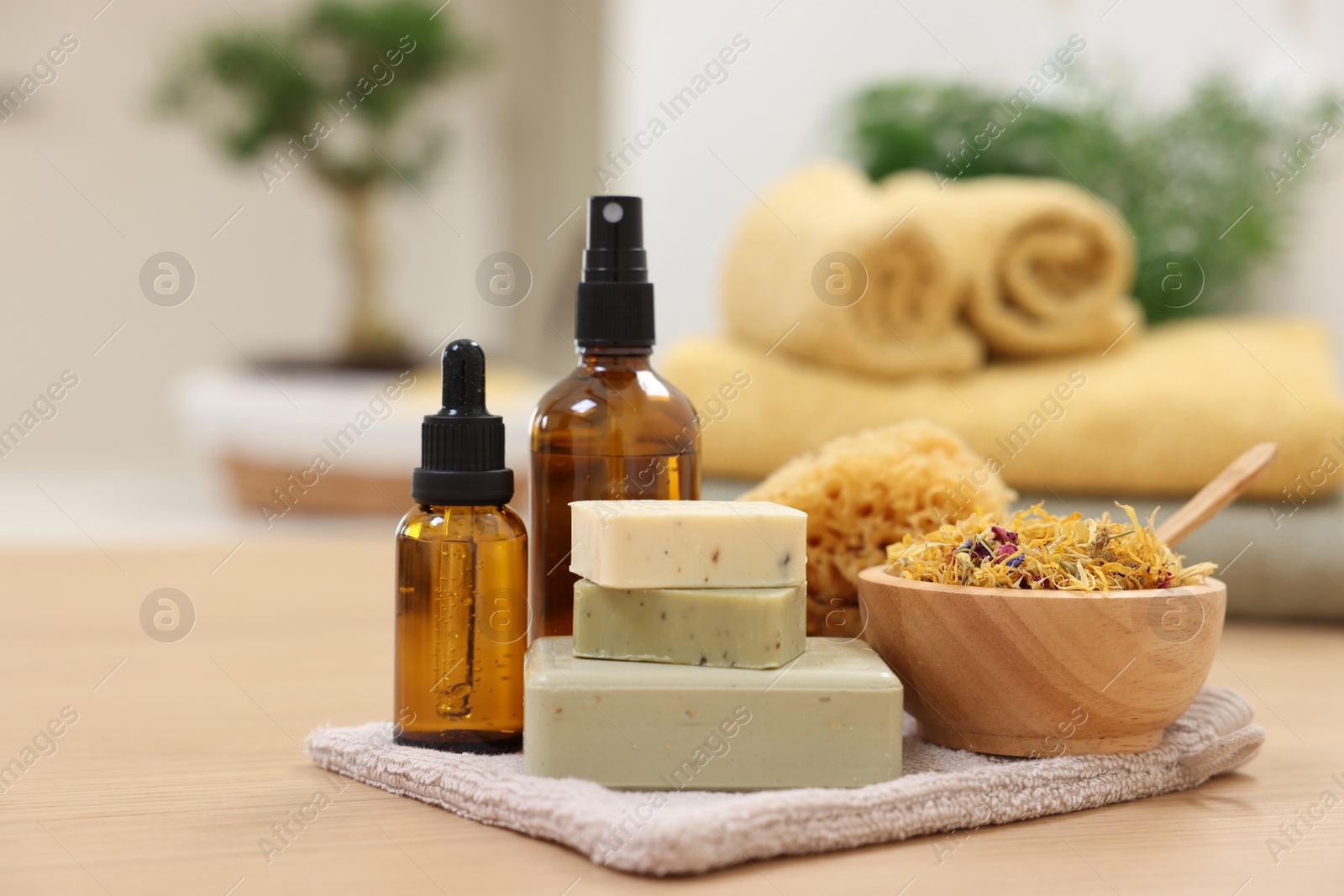Photo of Bottles of essential oils, bowl with dry flowers, soap bars and natural sponge on light wooden table. Spa therapy
