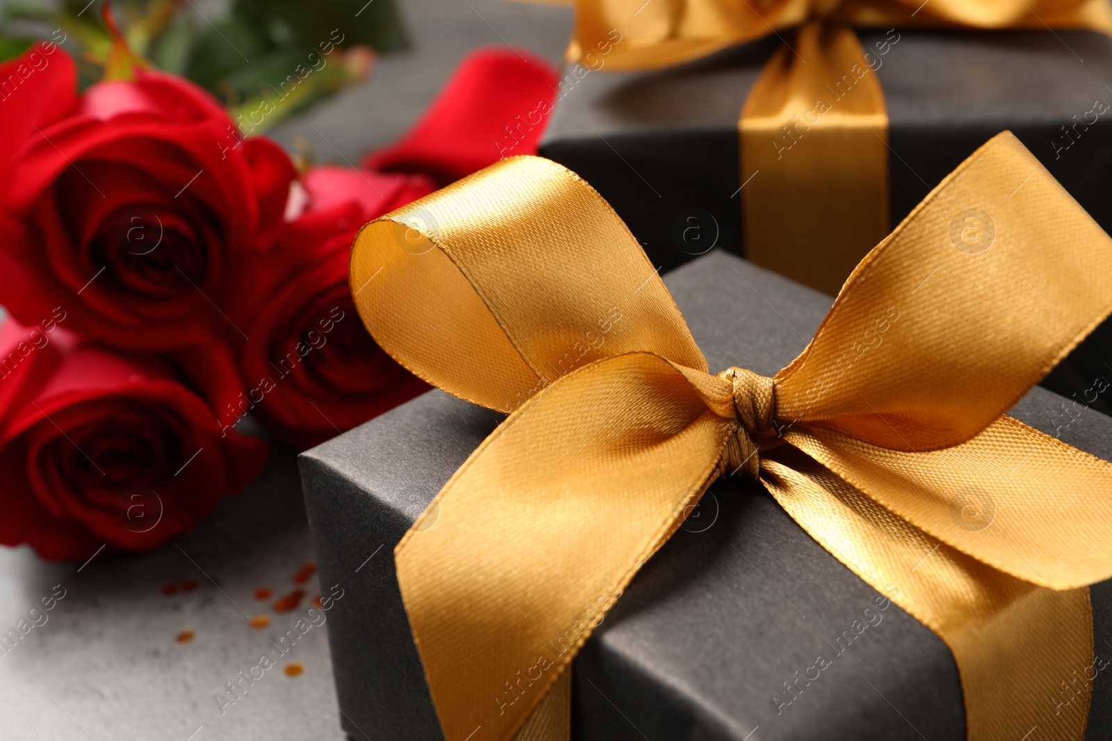 Photo of Black gift box and roses on grey table, closeup