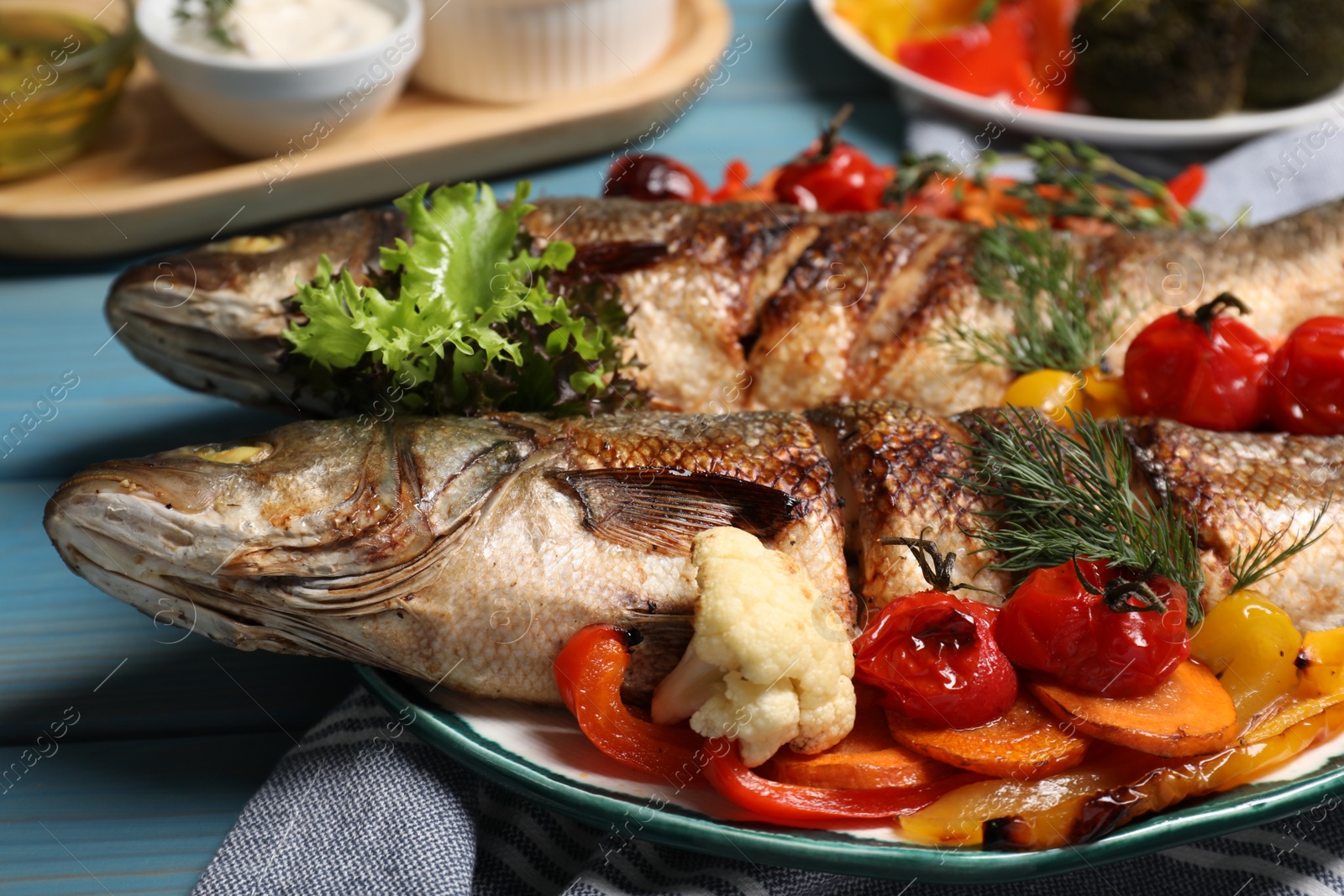 Photo of Plate with delicious roasted sea bass fish and vegetables on light blue wooden table, closeup