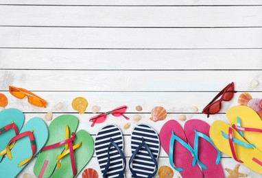 Photo of Many different stylish flip flops and sunglasses on white wooden background, flat lay. Space for text