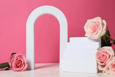 Photo of Stylish presentation for product. Geometric figures and beautiful roses on light table against pink background