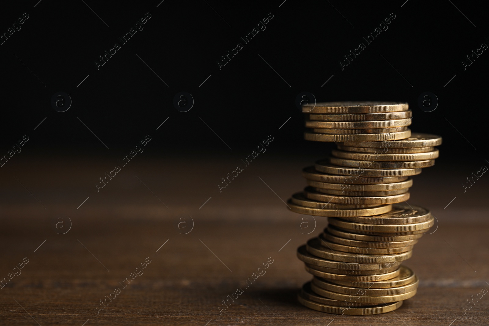 Photo of Many coins stacked on wooden table against black background, space for text