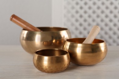 Golden singing bowls with mallets on white wooden table