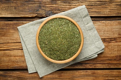 Photo of Bowl of dried dill on wooden table, top view