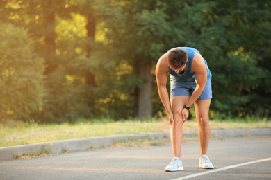 Photo of Young man in sportswear having knee problems in park