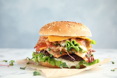 Photo of Tasty burger with bacon on table against color background