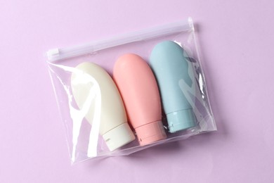 Photo of Cosmetic travel kit in plastic bag on violet background, top view