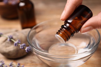 Photo of Woman dripping lavender essential oil from bottle into bowl at wooden table, closeup. Space for text