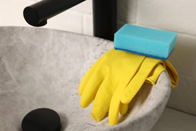 Photo of Sponge and rubber gloves on bathroom sink indoors, closeup