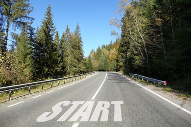Image of Asphalt road with word Start surrounded by forest on sunny day