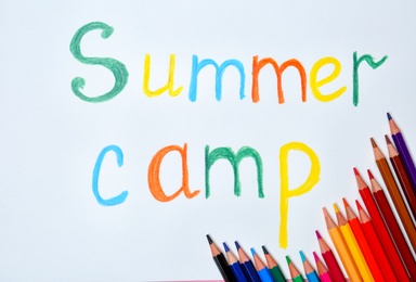 Photo of Colorful pencils and words SUMMER CAMP on white background, top view