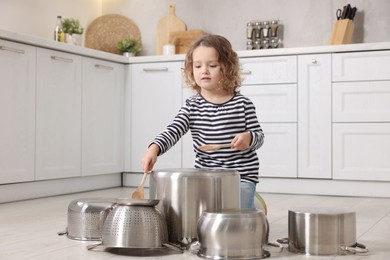 Little girl pretending to play drums on pots in kitchen