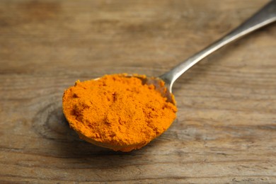 Photo of Spoon with saffron powder on wooden table, closeup