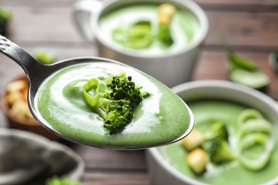 Photo of Spoon with fresh vegetable detox soup made of broccoli on blurred background, closeup