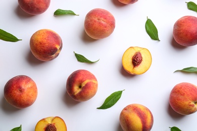 Photo of Fresh ripe peaches and green leaves on white background, flat lay