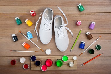 Photo of White sneakers and painting supplies on wooden table, flat lay. Customized shoes