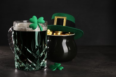 Photo of St. Patrick's day celebration. Green beer, leprechaun hat, pot of gold and decorative clover leaves on grey table. Space for text