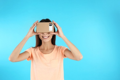 Young woman using cardboard virtual reality headset on color background. Space for text