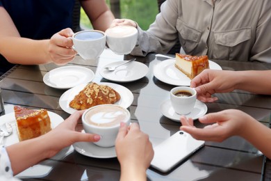 Photo of Friends drinking coffee at wooden table in outdoor cafe, closeup