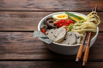 Photo of Delicious ramen with meat in bowl and chopsticks on wooden table, space for text. Noodle soup
