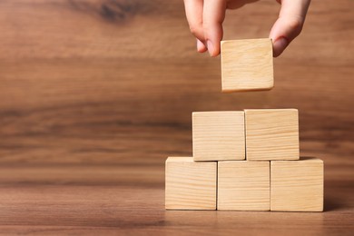 Photo of Woman building pyramid of cubes on wooden background, closeup with space for text. Idea concept