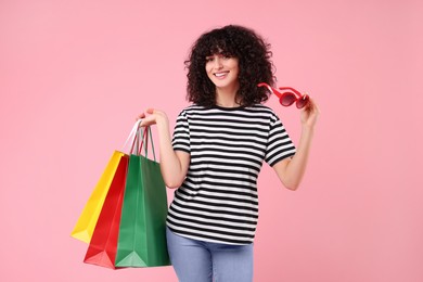Photo of Happy young woman with shopping bags and stylish sunglasses on pink background