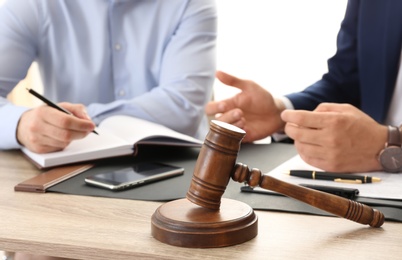 Photo of Gavel and blurred lawyer working with client on background